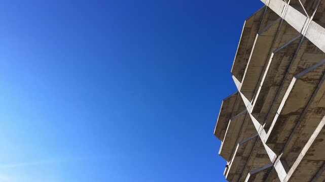 Low angle architectural shot of protruding concrete slabs and corners of a residential project. Corner of unfinished concrete building against clear blue sky. Aerial.