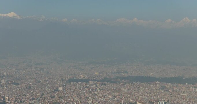 Drone shot of Kathmandu Nepal covered in heavy haze with dense city below and Himalayan peaks visible in the distance, showing low visibility and polluted atmosphere.
