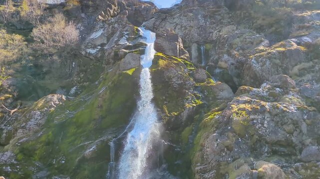 Powerful Cascading Waterfall Flowing Down Moss-Covered Rocky Cliff at Briksdal Glacier Norway - Sunny Day