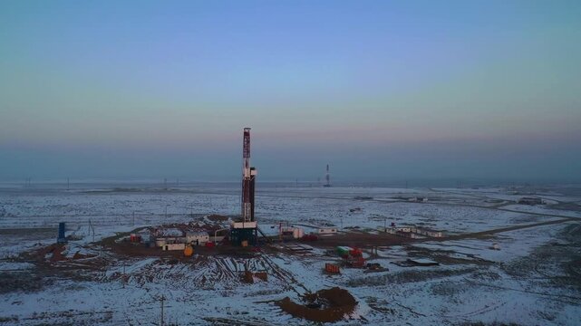 Remote oil drilling rig standing across snow-covered industrial field.