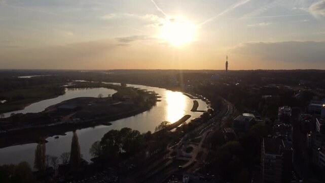 Nederrijn river in Arnhem Gelderland Netherlands within Rhine delta system with KEMA Tower and riverside arterial road along embankment and roundabout drone rising shot