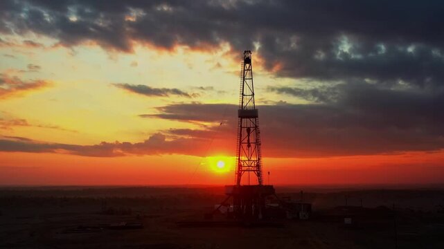 Oil drilling rig silhouette at sunset in desert landscape with dramatic sky.