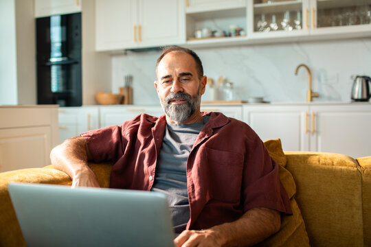 Middle-aged man working on laptop at home in modern kitchen