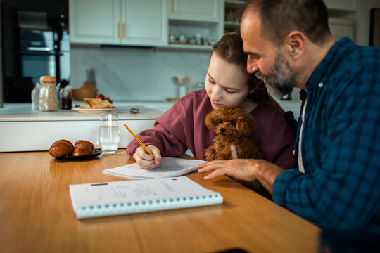 Parent helping child with homework at kitchen table with puppy