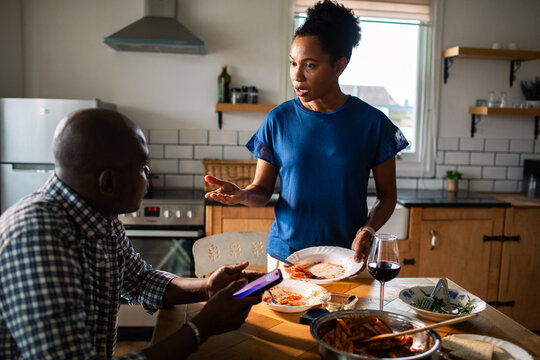 Couple arguing about smartphone during dinner in home kitchen