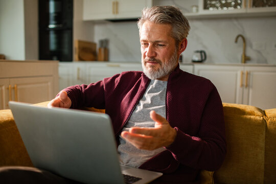 Mature man video calling on laptop in home kitchen