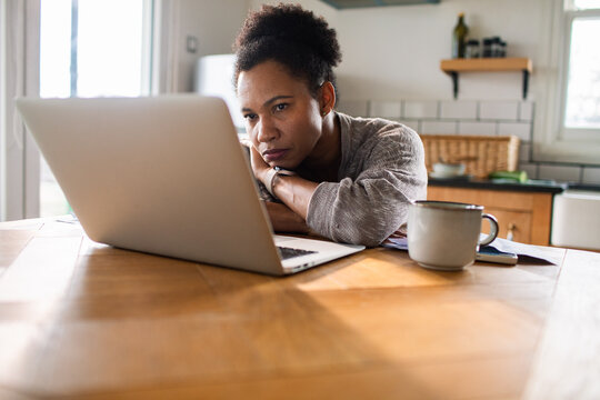 Woman working on laptop at home kitchen table