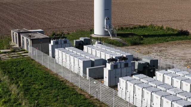 Aerial view of a modern bess, a battery energy storage system, at the base of a wind turbine, storing renewable power for the electricity grid and supporting sustainable energy solutions