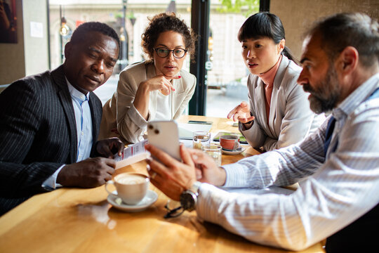 Four business colleagues reviewing smartphone during cafe meeting