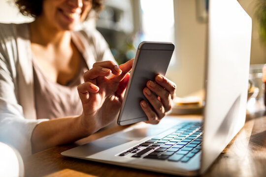 Smiling woman using smartphone at home office desk