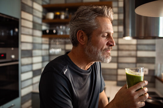 Mature man enjoying green smoothie in home kitchen