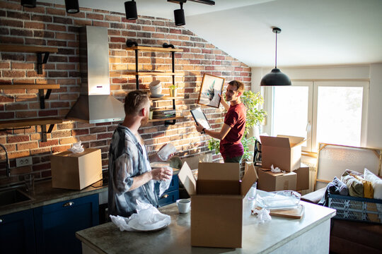 Two young men unpacking boxes and decorating a loft kitchen at home