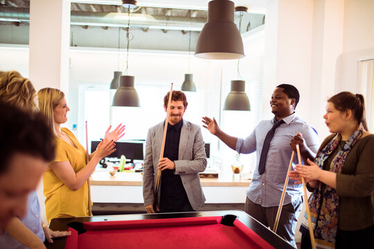 Coworkers playing pool in modern office break room