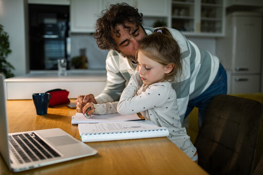 Father helping daughter with homework at kitchen table