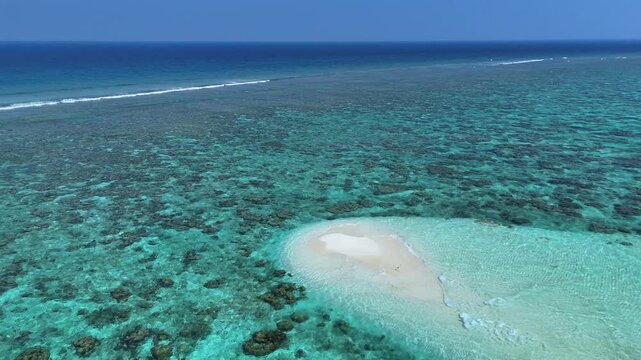 Aerial view of a small white sandbank surrounded by turquoise coral reefs and the deep blue Indian Ocean in Thoddoo, Alif Alif Atoll, Maldives.