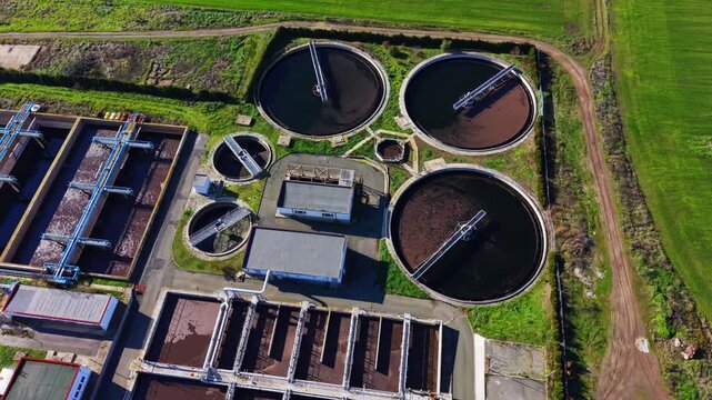 High angle overhead shot of several round settling tanks and rectangular aeration basins at a wastewater processing station. Top down view of circular clarifiers at water treatment facility.
