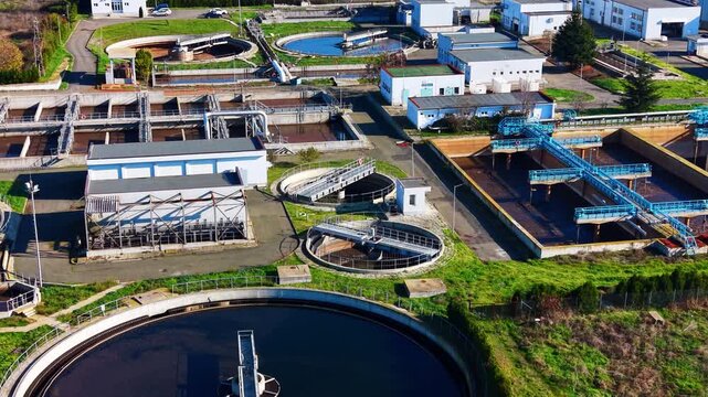 Detailed view of various industrial basins, pipes, and walkways within a modern sewage purification complex. Aerial shot of wastewater treatment tanks and pipes.