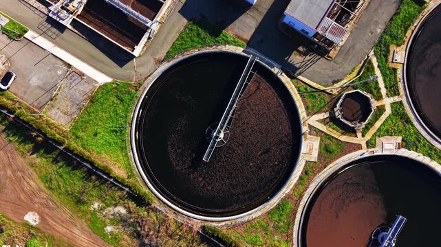 A circular settling tank with rotating scraper bridge and dark water. Aerial view of primary clarifier tank in sewage plant.