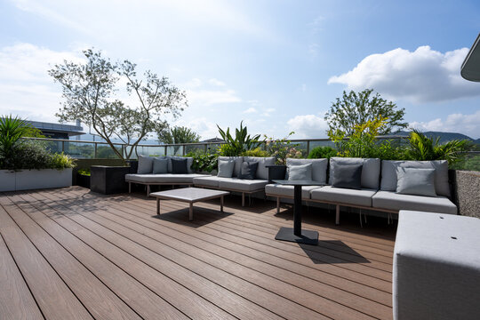 Modern rooftop terrace with gray sofas, green plants, and wooden deck under sunny daylight