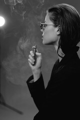 Fototapeta premium Black and white profile of a woman smoking, wearing glasses and dark clothing in a moody atmosphere.