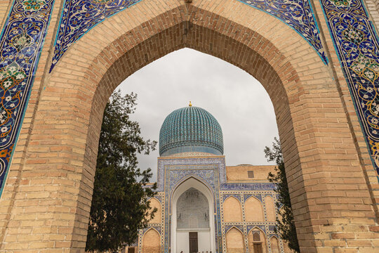 The blue dome of the Gur-e-Amir Mausoleum framed by a historic brick archway, showing the contrast between brick and tilework.