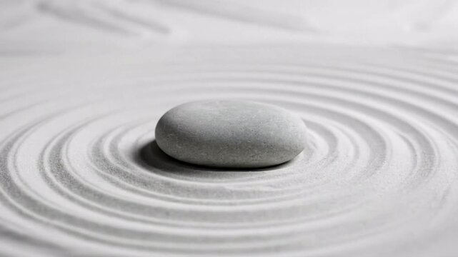 Single grey stone centered on raked white sand with circular ripples, symbolizing zen garden tranquility and mindfulness