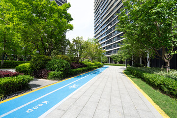 Modern high-rise buildings alongside a green urban pathway with blue cycling lane markings and lush landscaping © zhu difeng