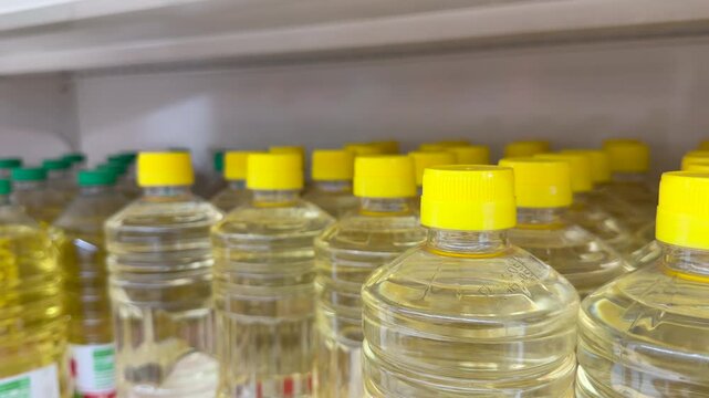 Rows of sunflower oil bottles with yellow caps displayed on retail shelf in supermarket product arrangement. Cooking oil retail footage suits FMCG brand promotion, grocery store, food supply chain