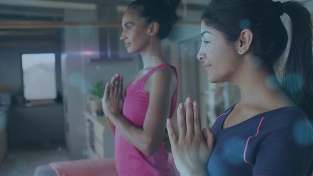 Two women holding prayer pose starting meditation for wellness in home, bokeh drifting across hands