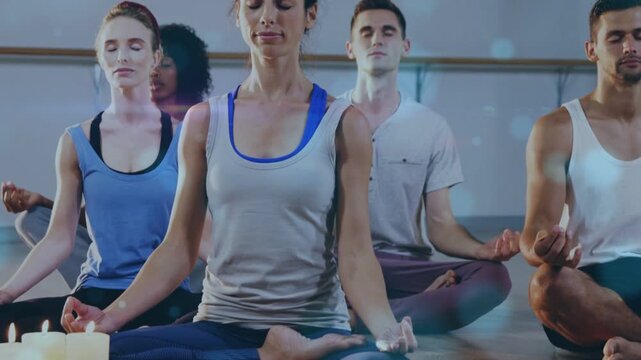 Centered woman and peers following guided cue, sitting on mats with candles, breathing for yoga