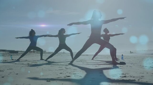 Four women stepping into yoga lunge on beach, holding form for fitness while bokeh crossing shadows