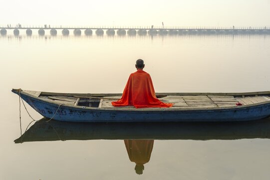 Sadhu with red shawl on a boat on the Ganges river at sunrise, Allahabad Kumbh Mela, world's largest religious gathering, Uttar Pradesh, India