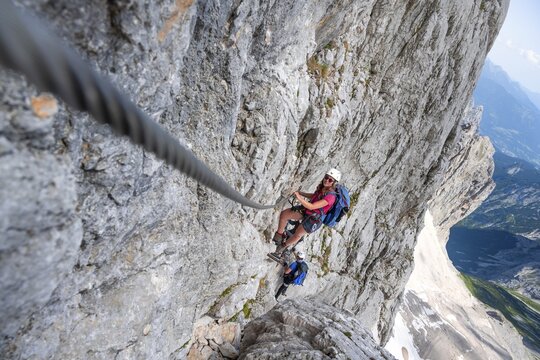 Mountaineer with helmet climbing in a secured via ferrata, Zugspitz via ferrata, ascent to the Zugspitze, view of mountain basin with snowfield of the H&ouml;llentalferner and H&ouml;llental, Wetterstein range, Wetterstein range, Bavaria, Germany