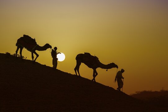 Two Rabari men going down a dune at sunset, silhouettes, Great Rann of Kutch, Gujarat, India