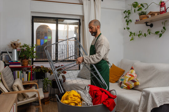 Bearded hispanic man setting up laundry drying rack at home