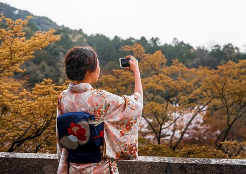 Japanese woman dressed with kimono, photographed with a mobile phone, at Kiyomizu-dera Temple, Higashiyama, Kyoto, Japan