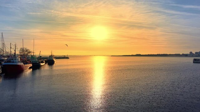 Fishing boats at sunset with sun path reflecting on the sea surface. Sun reflection on water in a peaceful harbor. Aerial view.