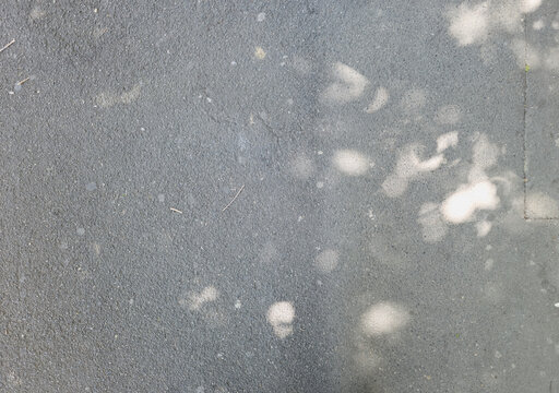 High-angle view of dark gray asphalt texture with dappled sunlight and soft tree shadows.
