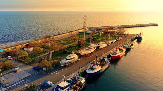 High angle view of various vessels lined up at the harbor during warm evening light. Fishing boats and yachts docked at sunset pier.