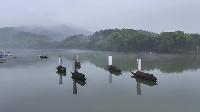 Bamboo rafts with fishing nets quietly moored on misty river surface with green mountains reflected in calm water