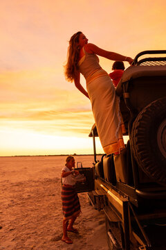 siblings on roof of safari vehicle looking at glorious sunset over Makgadikgadi Park, Botswana, Africa
