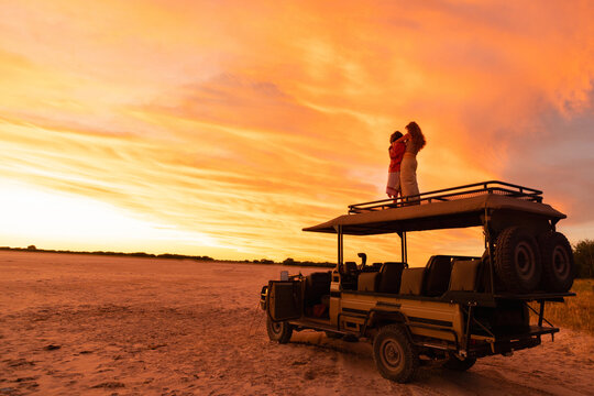 siblings on roof of safari vehicle looking at glorious sunset over Makgadikgadi Park, Botswana, Africa