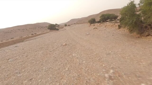 FPV drone flight over vast, rocky desert landscape during hazy sunset near Tan-Tan, Morocco. Aerial, copy space