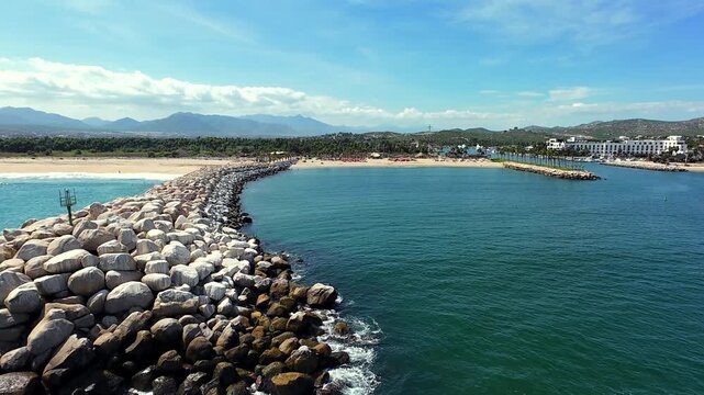 Drone flying alongside a breakwater at the San Jos&eacute; del Cabo Marina, heading toward Veleros Beach and the marina.