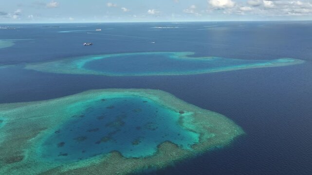 Aerial view of vibrant turquoise coral reefs and atolls surrounded by the deep blue Indian Ocean under a clear sky in Gulhi, Kaafu Atoll, Maldives.