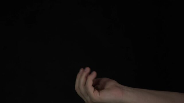 Close-up of a hand against a black background throwing up a gold coin and catching it
