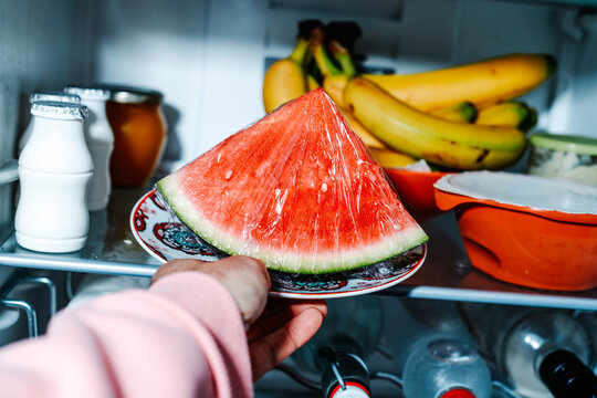 man placing a plate with watermelon in the fridge