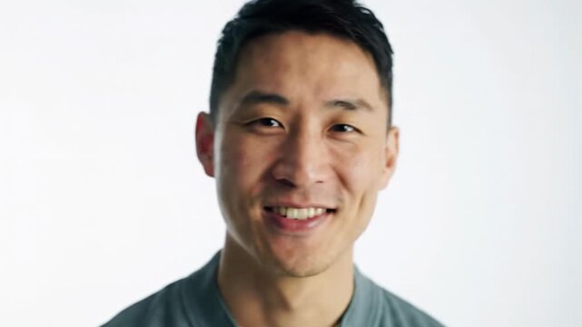 Well-composed medium close-up video of a charismatic young man with neat grooming in smart-casual attire, smiling against a white studio background with soft bokeh, radiating positivity and brand