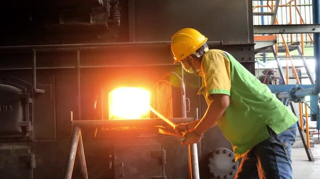 Industrial worker stoking a hot furnace in a manufacturing plant, professional stoker operating a heavy duty boiler in a factory