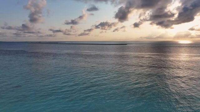 Aerial view of the turquoise ocean waters and a distant sandbar under a cloudy sunset sky at Gulhi, Kaafu Atoll, Maldives.